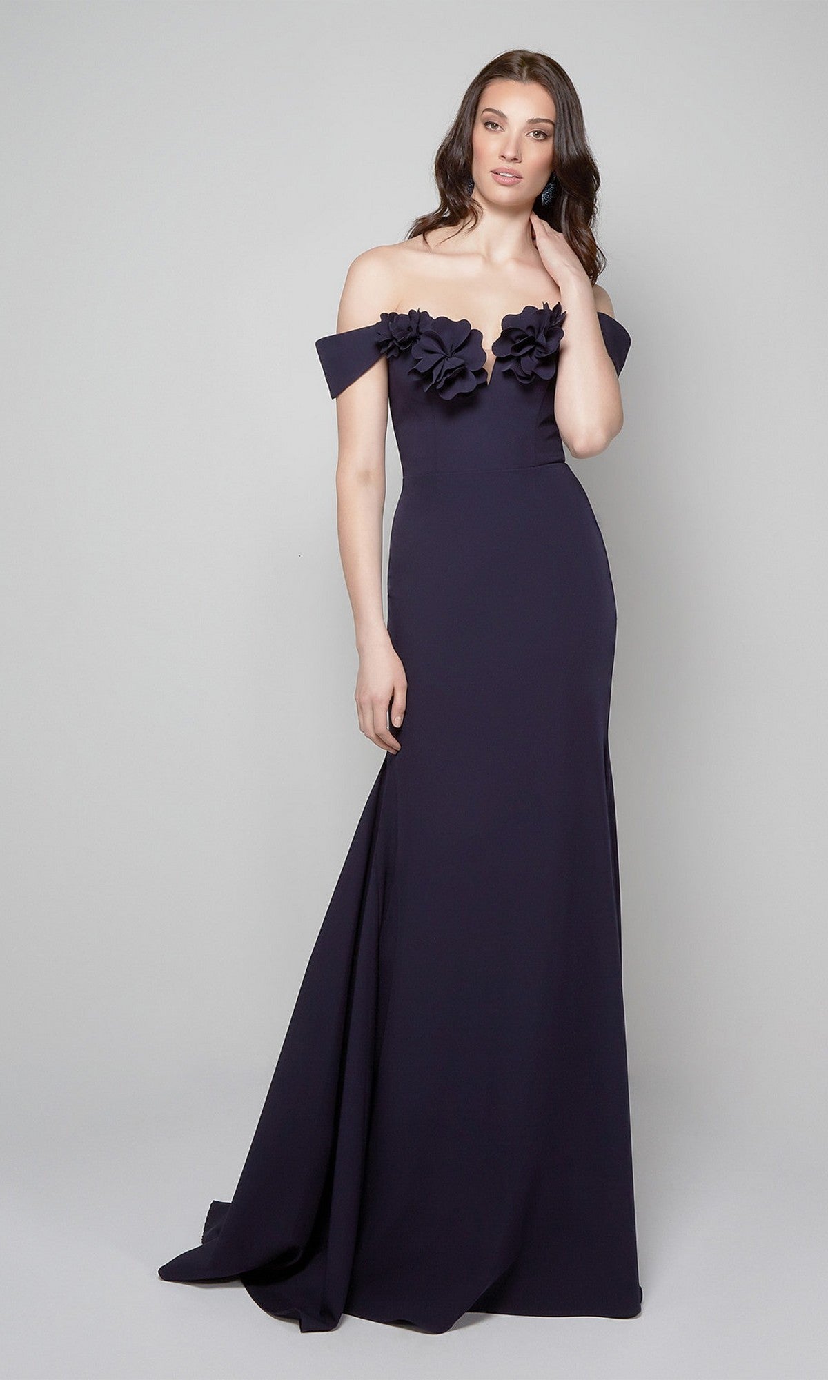 A woman wears the Alyce 7062 long navy formal dress with off-the-shoulder sleeves and 3D floral bodice accents, standing against a light gray background—ideal for elegant evening events.